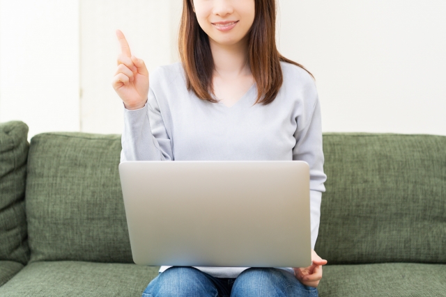 ノートパソコンを膝に乗せて人差し指を上に立てている女性
